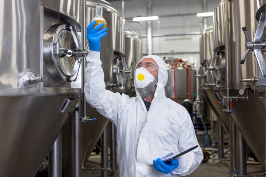 A person in a white protective suit and mask holding a beaker