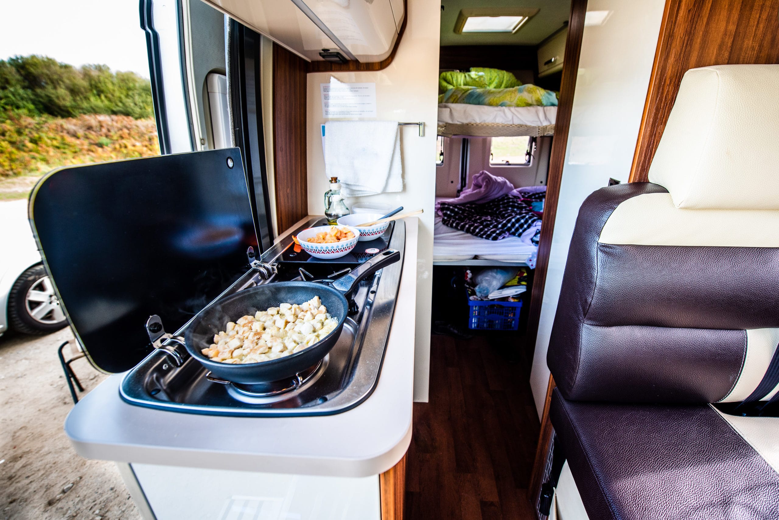 Cooking dinner or lunch in campervan, motorhome or RV. Preparing chicken in a pan in camper van when traveling with RV, motor home caravan or motorvan. Vanlife or van life lifestyle on the road.