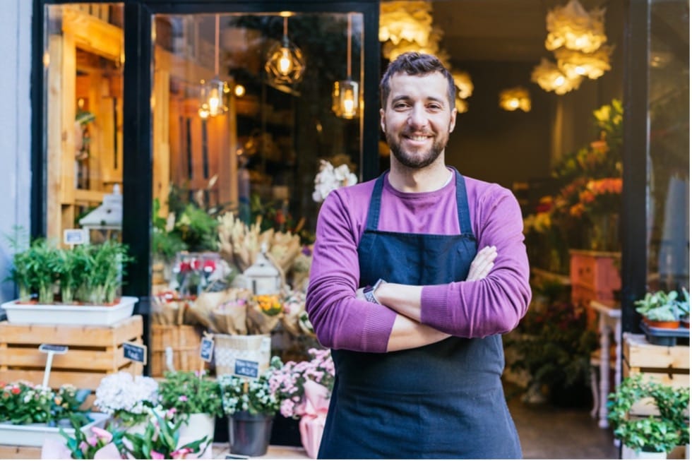 A person wearing a black apron standing in front of a flower shop