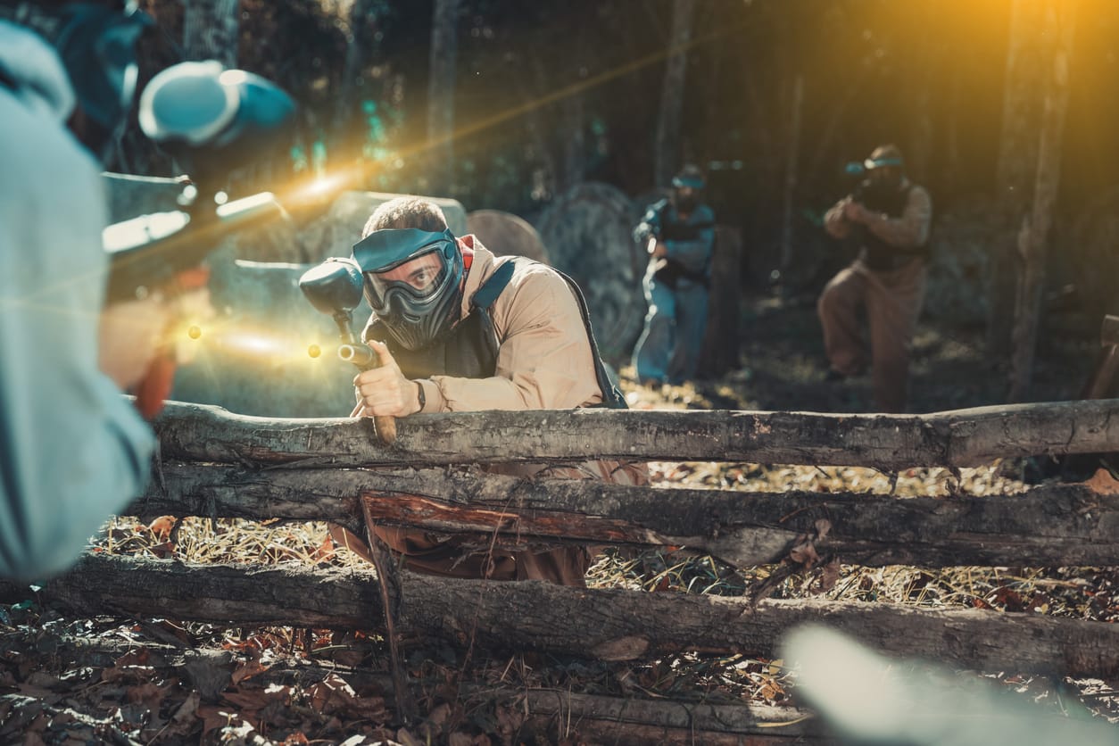 Team of male and female paintball players with marker guns aiming on gamefield outdoors