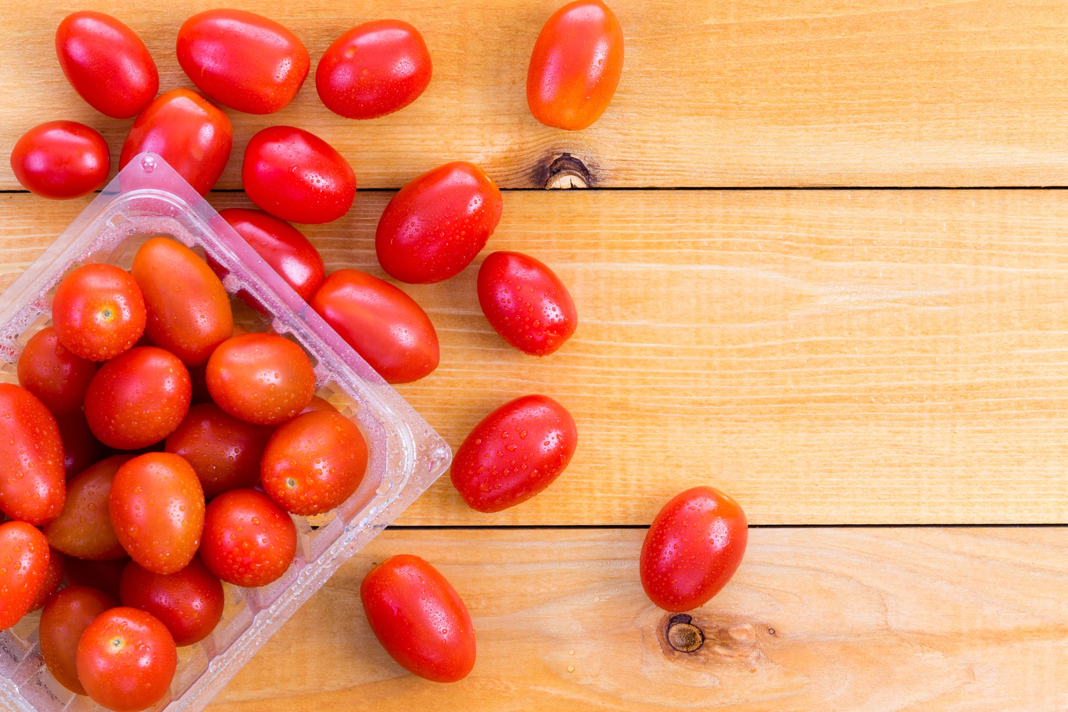 Punnet of fresh healthy baby tomatoes displayed on a wooden table with some spread around alongside , copy space to the side